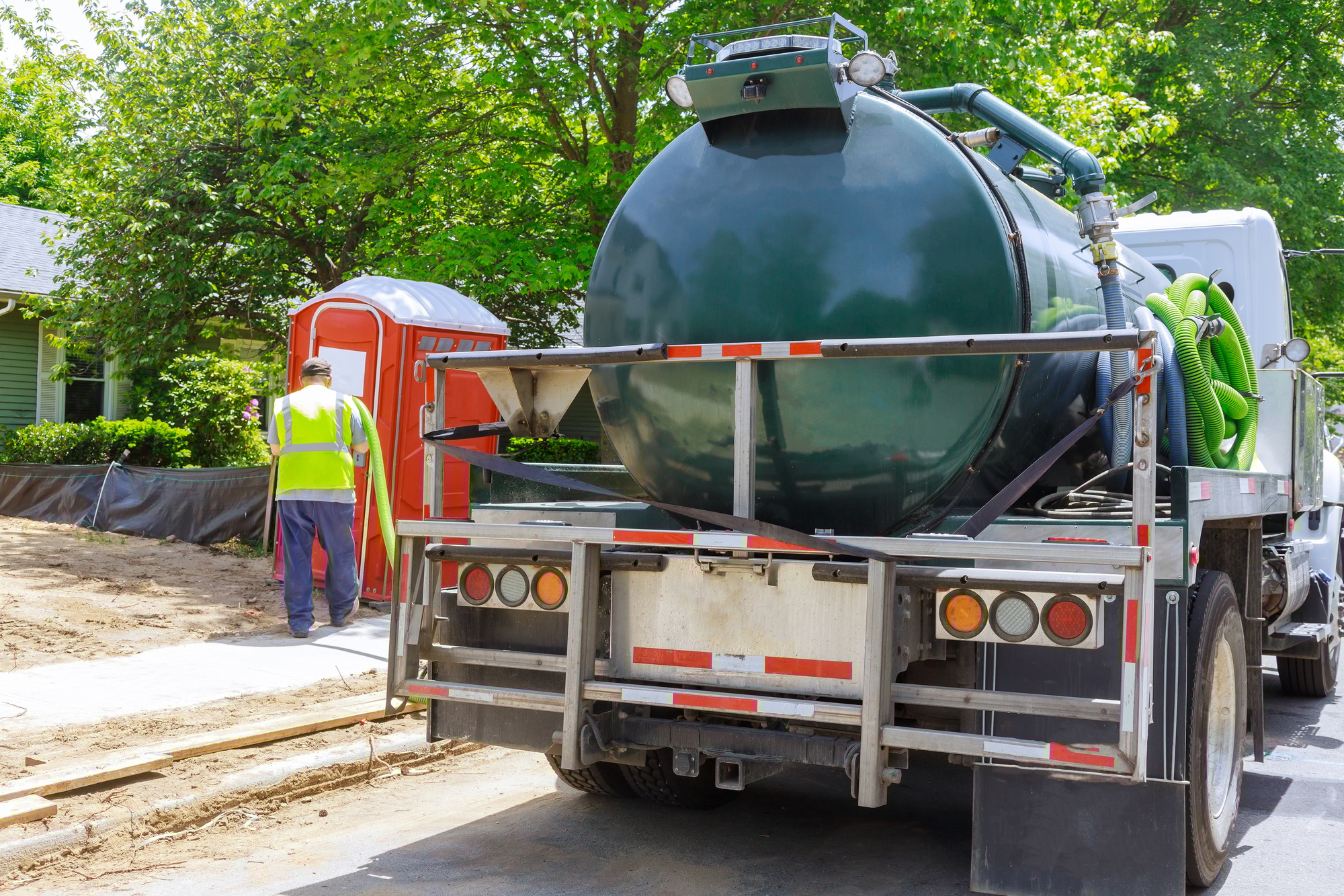 Sewage truck on worker pumping feces out of rental toilet for disposal and cleaning at the