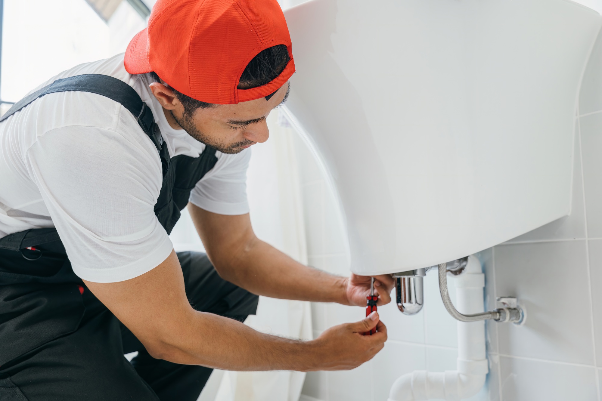 With a wrench in hand a technician fixes a water pipe under a bathroom sink. This plumber service